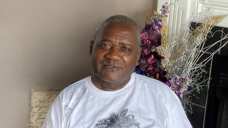 Person seated indoors with floral decorations in the background.